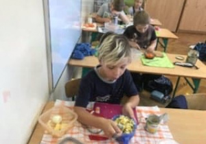 Uczniowie robią sałatki przy stolikach w klasie